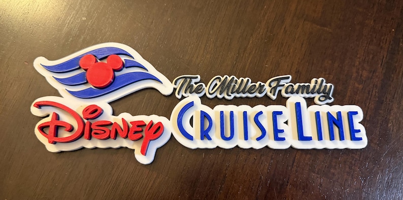 May include: A white 3D printed sign with the text "Disney Cruise Line" in blue and red letters. The sign also includes a blue and white Mickey Mouse ship logo and the text "The Miller Family" in black.
