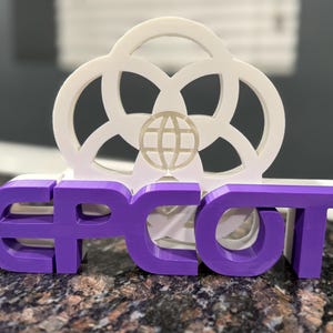 May include: A purple 3D printed sign that says "EPCOT" with a white 3D printed globe and circle design on top.