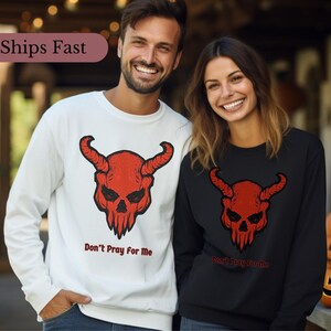 Peut inclure: Deux sweat-shirts à manches longues, un blanc et un noir, avec un motif de crâne de diable rouge et le texte "Ne priez pas pour moi".