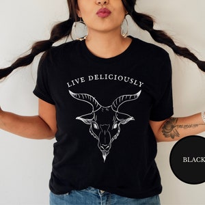 A hispanic bruja witch wearing a black emo trad goth witchcraft shirt in an occult pagan satanic style featuring the demonic goat, black phillip