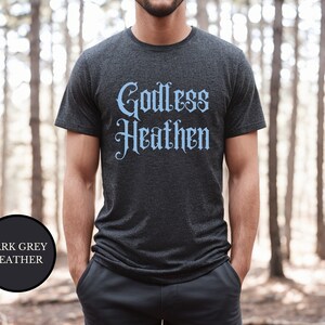 Man in woods wearing an anti religion shirt that says Godless Heathen in gothic pastel blue font on a grey shirt