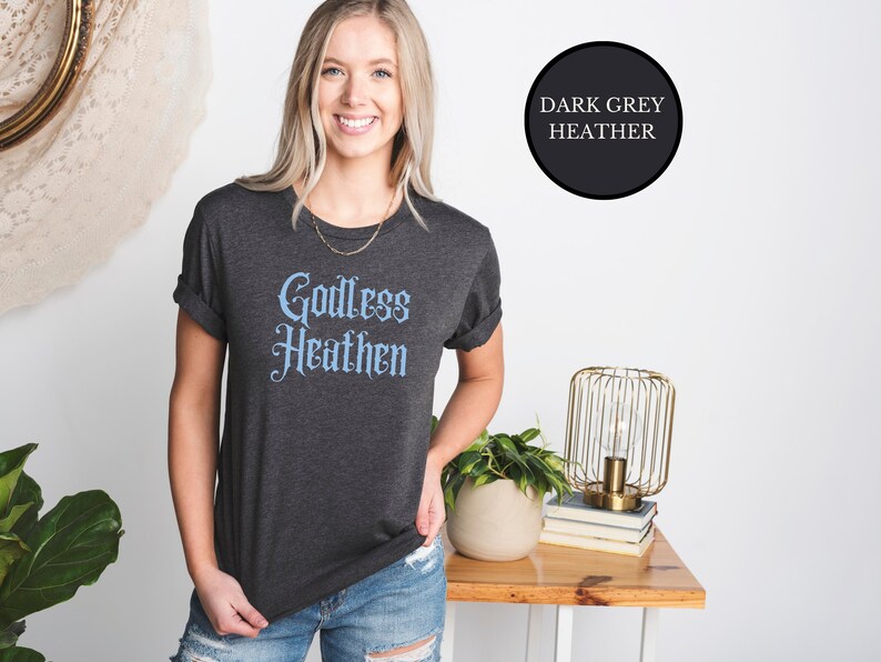 witch girl wearing an anti religion shirt that says Godless Heathen in gothic pastel blue font on a grey shirt