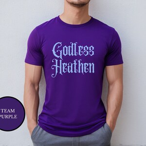 Gay man wearing an anti religion shirt that says Godless Heathen in gothic pastel blue font on a purple shirt