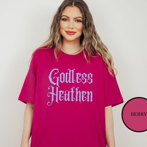 Hippie witch girl wearing an anti church shirt that says Godless Heathen in gothic pastel blue font on a pink shirt