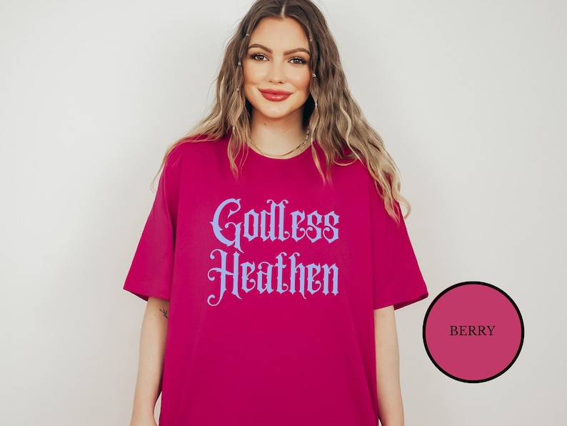 Hippie witch girl wearing an anti church shirt that says Godless Heathen in gothic pastel blue font on a pink shirt