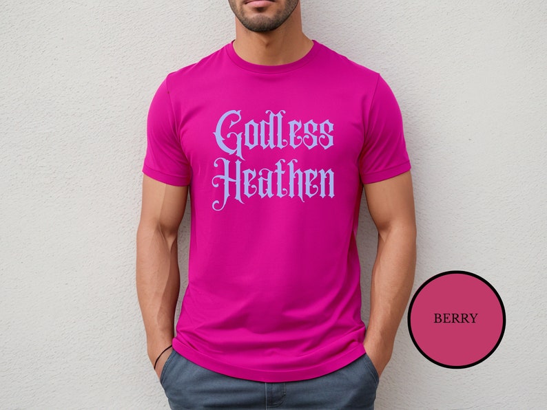 Leftist male wearing an anti religion shirt that says Godless Heathen in gothic pastel blue font on a pink shirt