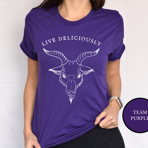 Asian witch wearing a haunting purple witchcraft vibes tee shirt that reads Live Deliciously with an evil Baphomet goat head on the chest ofthis horror film shirt