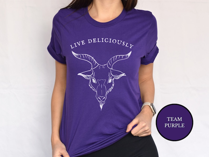Asian witch wearing a haunting purple witchcraft vibes tee shirt that reads Live Deliciously with an evil Baphomet goat head on the chest ofthis horror film shirt