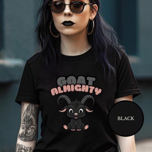 Puede incluir: Camiseta negra con una cabra negra de dibujos animados con detalles rosas y el texto "GOAT ALMIGHTY" en letras rosas y grises.