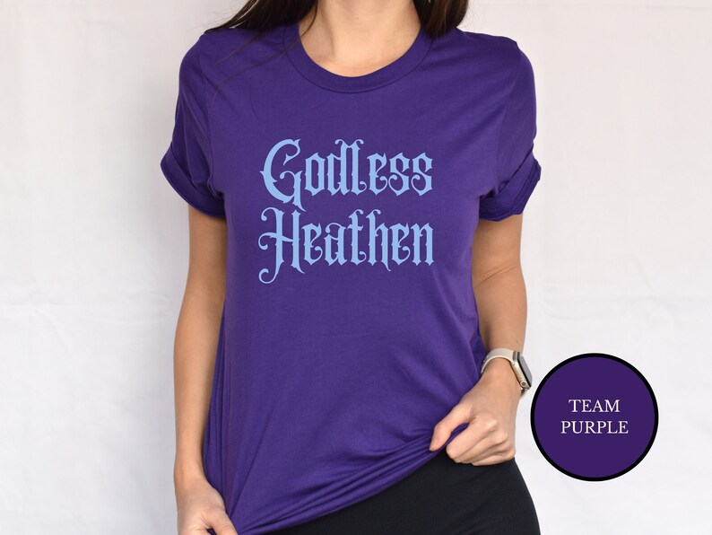 Asian witch girl wearing an anti religion shirt that says Godless Heathen in gothic pastel blue font on a purple shirt