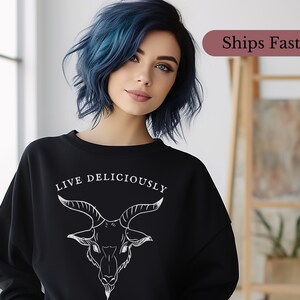 emo goth egirl witch wearing a witchcraft Black Phillip sweatshirt that reads Live Deliciously and features a demonic Baphomet goat head on the front