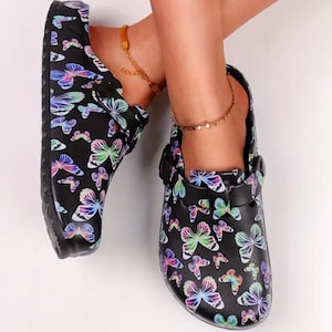 May include: Black slip-on clogs with a butterfly print. The clogs have a buckle closure and a comfortable design.