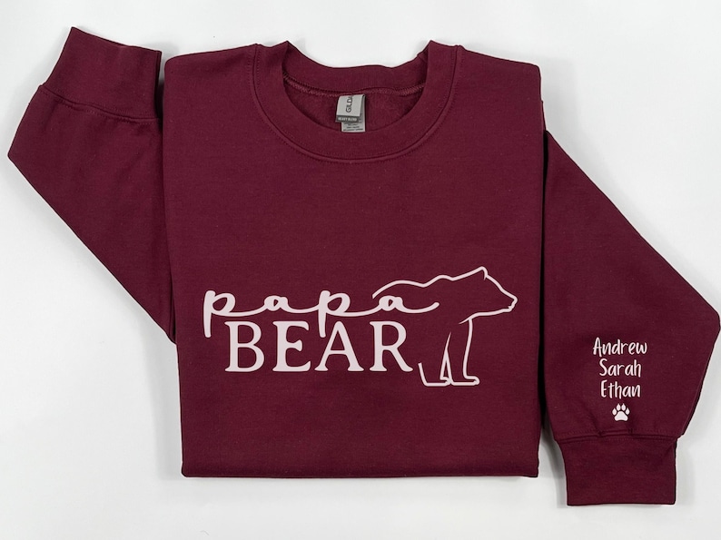 May include: A maroon sweatshirt with the words "papa BEAR" in white script and a bear outline. The right sleeve has the names "Andrew Sarah Ethan" and a paw print in white.