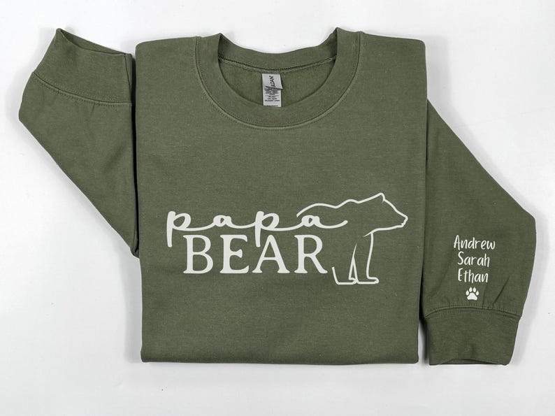 May include: Olive green sweatshirt with the words "Papa Bear" and a bear graphic in white. The sleeve has the names "Andrew, Sarah, Ethan" and a paw print.