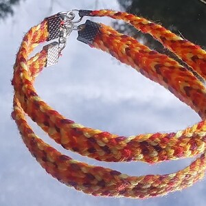 May include: Two braided bracelets in orange, yellow, and red colors with silver clasps.