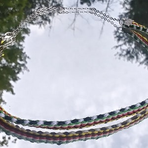 May include: A double-layered necklace with a silver chain and a braided cord. The cord is made of red, yellow, green, white, and black threads.