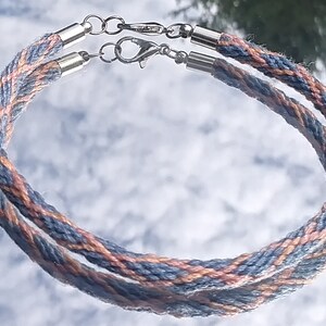 May include: A double-strand bracelet made of braided cord in shades of blue and peach. The bracelet has silver-toned clasps.