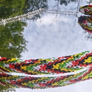 May include: A multi-colored braided necklace with a silver chain. The necklace is made of red, yellow, green, black, and white string.