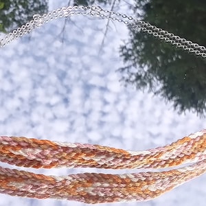 May include: A woven necklace with a silver chain and clasp. The necklace is made of orange, pink, and white threads.