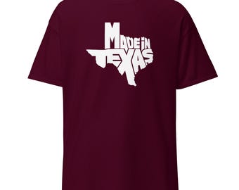 May include: A maroon t-shirt featuring a white outline of the state of Texas with the words "Made in Texas" printed inside the shape. The shirt has short sleeves and a crew neck.