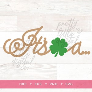 May include: A brown cursive design that says "It's a..." with a green four-leaf clover in the middle. The design is on a white wood background.