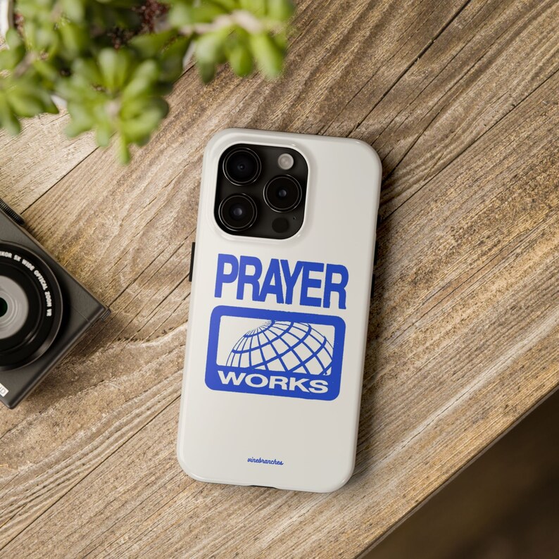May include: White iPhone case with a blue logo that says "PRAYER WORKS" and a globe inside the logo.