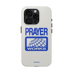 May include: White iPhone case featuring a blue graphic that reads "PRAYER WORKS" and a globe icon. The case has a black camera bump and a black border.