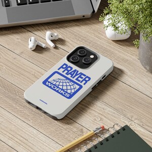 May include: White iPhone case with a blue logo that says "PRAYER WORKS" and a globe graphic. The case has a black bumper and a camera lens cutout.