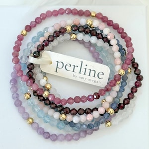 Puede incluir: Conjunto de pulseras de cuentas en tonos rosa, morado, azul y blanco, con detalles dorados. Las pulseras están hechas de pequeñas cuentas redondas. Una etiqueta con la palabra "perline" está adjunta.