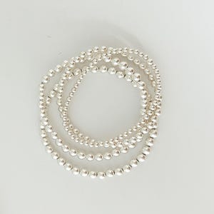 May include: A set of three silver bead bracelets, stacked on top of each other. The bracelets are made of small, round beads.