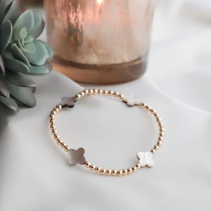 May include: A gold beaded bracelet with four white and brown clover charms.