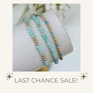 May include: Three beaded bracelets featuring alternating light blue faceted gemstone beads and small metallic gold-tone spherical beads. The bracelets are arranged in a row, showcasing a consistent pattern of blue and gold elements throughout.