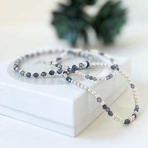 May include: Three silver bracelets with blue gemstone beads. The bracelets are stacked on top of each other and are on a white surface.