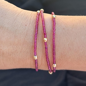 Pode incluir: Três pulseiras sobrepostas com pequenas contas cor-de-rosa e detalhes dourados.