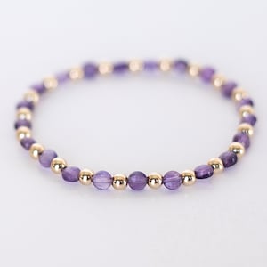 May include: A delicate bracelet made with small purple amethyst beads and gold beads.
