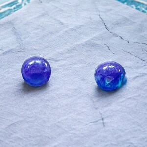 May include: Two blue glass marbles with iridescent swirls on a white surface.