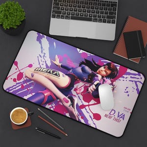 May include: A purple and pink gaming mouse pad with a white background. The mouse pad features a cartoon image of a female character from the video game Overwatch. The character is wearing a pink and blue suit and holding a gun. The text "D.VA NERF THIS!" is printed on the mouse pad.