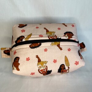 Puede incluir: Una bolsa rosa con cremallera con un patr&oacute;n repetido de una mujer polinesia de dibujos animados con piel morena y cabello negro. La mujer lleva un atuendo marr&oacute;n y amarillo y sostiene una pala.