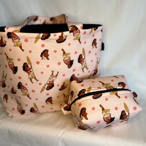 Puede incluir: Una bolsa de mano rosa y una bolsa de cosm&eacute;ticos rosa a juego con un patr&oacute;n de una mujer polinesia de dibujos animados sosteniendo una pala. El patr&oacute;n se repite en ambas bolsas.