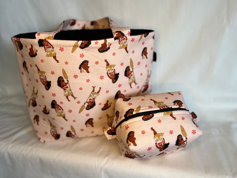 Puede incluir: Una bolsa de mano rosa y una bolsa de cosm&eacute;ticos rosa a juego con un patr&oacute;n de una mujer polinesia de dibujos animados sosteniendo una pala. El patr&oacute;n se repite en ambas bolsas.