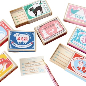 May include: A collection of rectangular matchboxes featuring colorful illustrations of animals including a black cat, white cat, sheep, rabbits, penguin, bear, and panda, with Japanese text and some boxes containing matches.