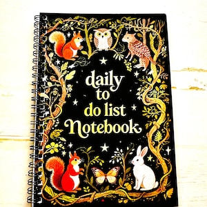 May include: A spiral-bound notebook with a black cover featuring the text "daily to do list Notebook". The cover is decorated with illustrations of a squirrel, owl, rabbit, butterfly, and other forest elements in gold and red.