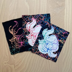 Könnte beinhalten: Drei quadratische Stoffkunstwerke mit floralen Designs. Jedes Stück hat ein anderes Farbschema: Schwarz mit Orange und Pink, Schwarz mit Rot und Weiß und Schwarz mit Blau und Lila. Der Hintergrund hat ein farbenfrohes, netzartiges Muster.