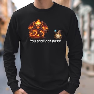 Puede incluir: Camiseta negra de manga larga con un gráfico de un demonio de fuego y un mago, con el texto "You shall not pass!" El demonio es rojo y naranja, y el mago sostiene un orbe azul.