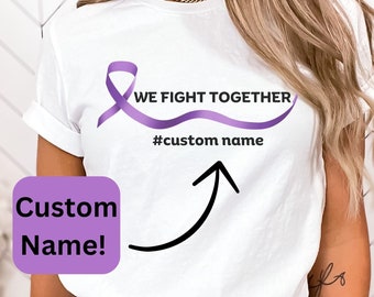 May include: White t-shirt featuring a purple ribbon design with the text "WE FIGHT TOGETHER" and "#custom name". A purple square with the words "Custom Name!" is in the lower left corner. A black arrow points to the text.