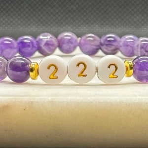 May include: A purple amethyst beaded bracelet with three white beads that have the number 2 on them in gold lettering.