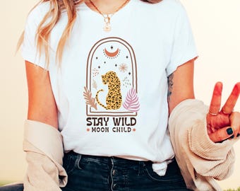 May include: White t-shirt with a graphic design featuring a leopard, a crescent moon, stars, and leaves. The text "Stay Wild Moon Child" is printed below the graphic.