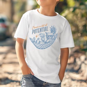 May include: White t-shirt featuring a blue and orange graphic of a cat in sunglasses relaxing in a hammock with a cocktail and pineapple. The text "I have a lot of POTENTIAL" is above the cat.