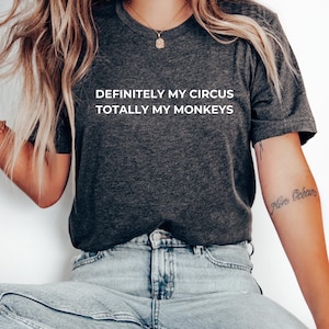 Könnte beinhalten: Ein dunkelgraues T-Shirt mit weißem Text, der "Definitely my circus, totally my monkeys" lautet.