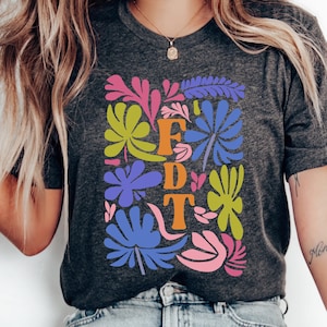Może przedstawiać: Szary t-shirt z kolorowym wzorem kwiatowym i literami "FDT" w kolorze pomarańczowym.